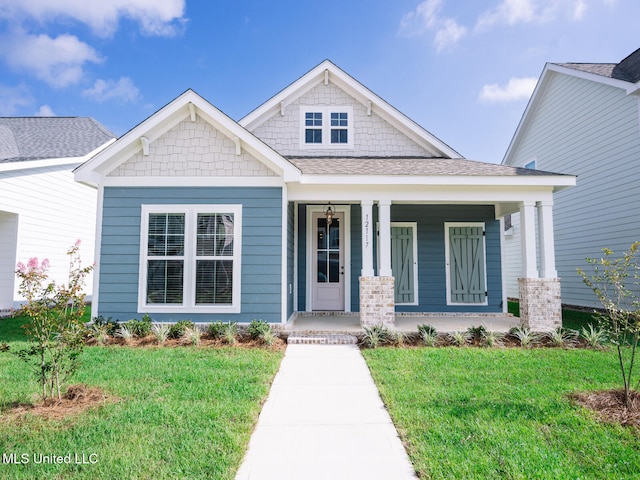 craftsman-style house with a front lawn, a shingled roof, and covered porch