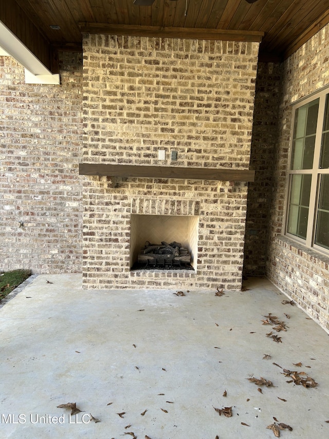 unfurnished living room with an outdoor brick fireplace, wood ceiling, and brick wall