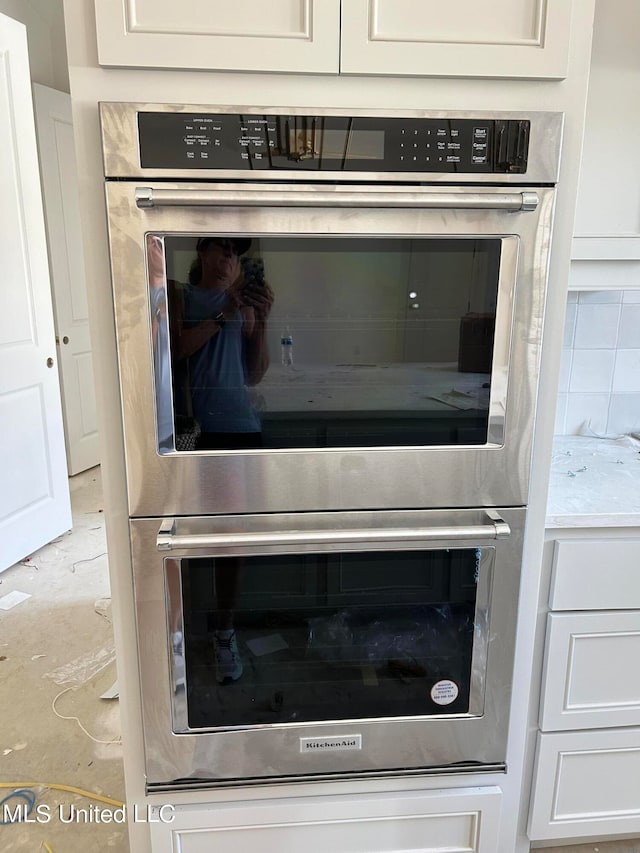 room details with white cabinets, backsplash, and double oven