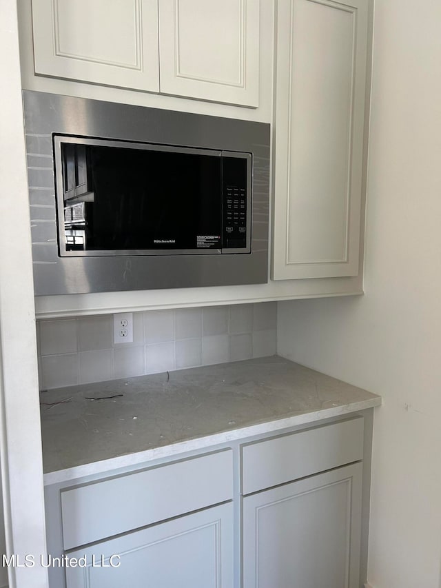 interior details with light stone countertops, tasteful backsplash, white cabinets, and stainless steel microwave