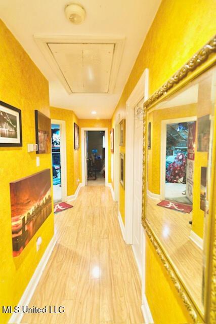 hall featuring baseboards, light wood finished floors, and attic access