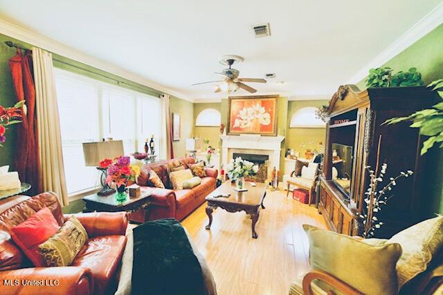 living room with crown molding, a fireplace, a ceiling fan, wood finished floors, and visible vents