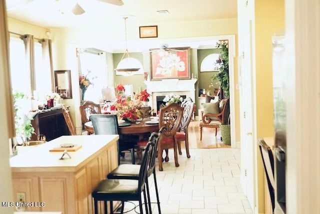 dining area with ceiling fan, a fireplace, and light tile patterned flooring