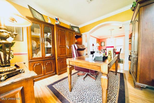 home office featuring crown molding, arched walkways, light wood-style flooring, and decorative columns