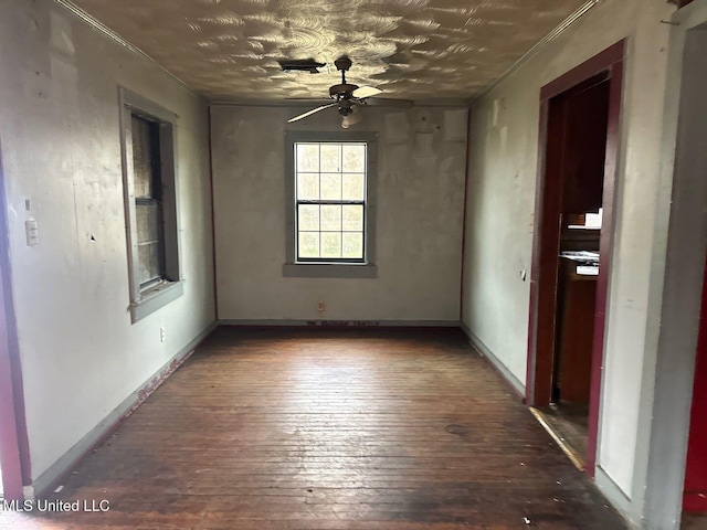 empty room featuring wood-type flooring, crown molding, baseboards, and a ceiling fan