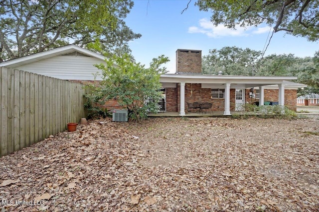 rear view of house with a chimney, covered porch, fence, central air condition unit, and brick siding