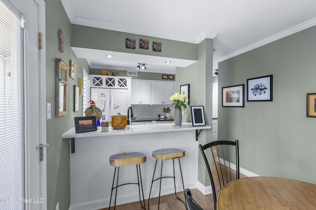 kitchen with backsplash, ornamental molding, white cabinetry, a kitchen bar, and kitchen peninsula