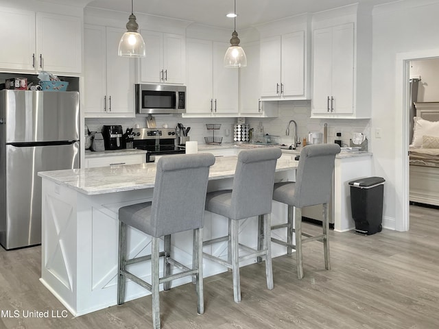 kitchen featuring pendant lighting, appliances with stainless steel finishes, a kitchen island with sink, white cabinetry, and light stone countertops