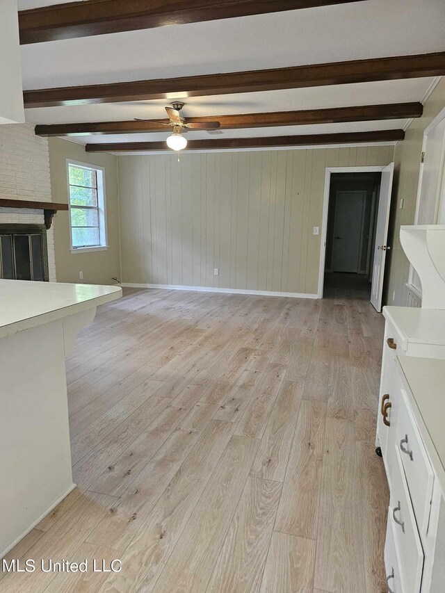 unfurnished living room with beamed ceiling, ceiling fan, a fireplace, and light hardwood / wood-style floors