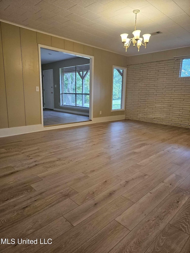 spare room featuring hardwood / wood-style flooring, plenty of natural light, brick wall, and a notable chandelier