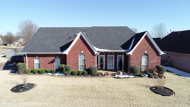 view of front facade with brick siding, a front lawn, and roof with shingles