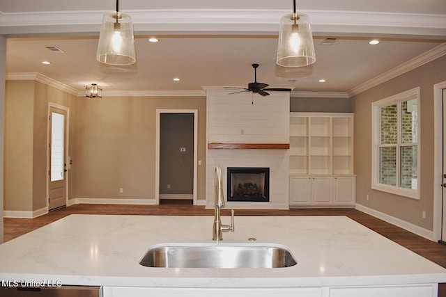 kitchen with light stone countertops, decorative light fixtures, a center island with sink, and sink