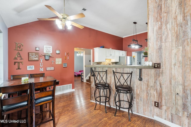 kitchen with kitchen peninsula, ceiling fan, a breakfast bar, stainless steel refrigerator, and dark wood-type flooring