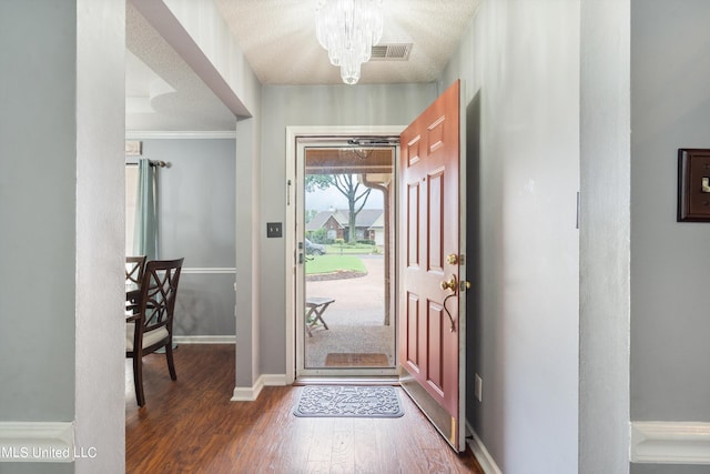 foyer with ornamental molding, a textured ceiling, dark hardwood / wood-style floors, and an inviting chandelier