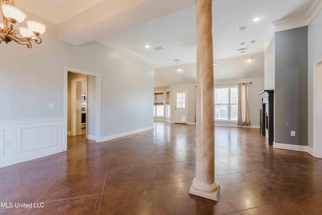 unfurnished living room featuring an inviting chandelier, crown molding, dark tile patterned floors, and ornate columns