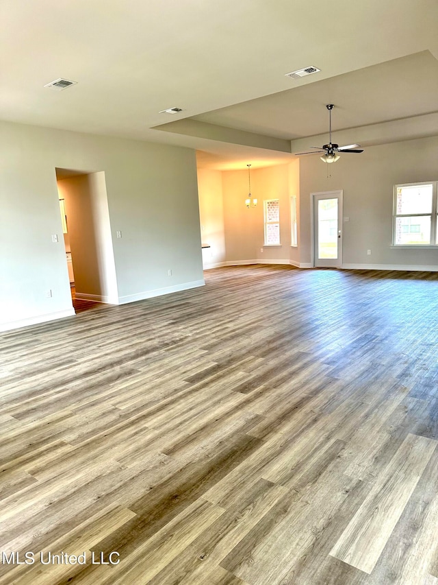 unfurnished living room featuring ceiling fan with notable chandelier and hardwood / wood-style flooring