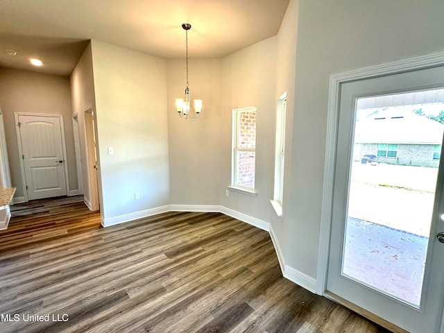 unfurnished dining area with a healthy amount of sunlight, dark hardwood / wood-style flooring, and an inviting chandelier