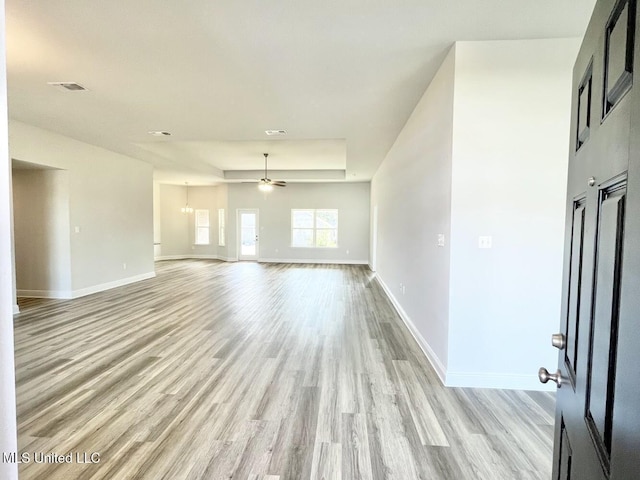 unfurnished room featuring light wood finished floors, a tray ceiling, baseboards, visible vents, and ceiling fan with notable chandelier