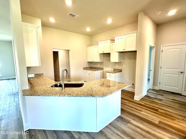 kitchen with light stone countertops, white cabinetry, sink, kitchen peninsula, and light hardwood / wood-style floors