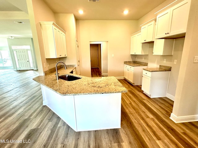 kitchen with hardwood / wood-style floors, white cabinets, sink, stone countertops, and kitchen peninsula