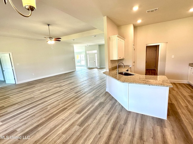 kitchen featuring sink, light hardwood / wood-style flooring, light stone countertops, white cabinetry, and kitchen peninsula