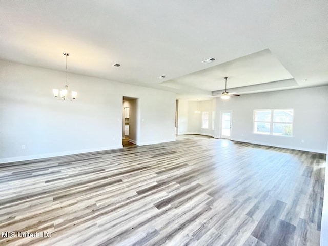 unfurnished living room with a tray ceiling, wood finished floors, visible vents, and baseboards