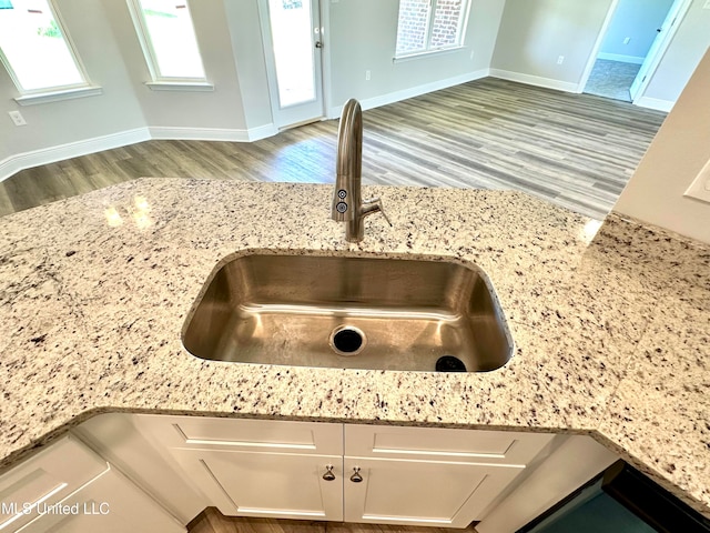 room details featuring white cabinetry, light stone counters, light wood-type flooring, and sink