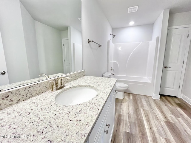 full bathroom featuring toilet, visible vents, wood finished floors, washtub / shower combination, and vanity