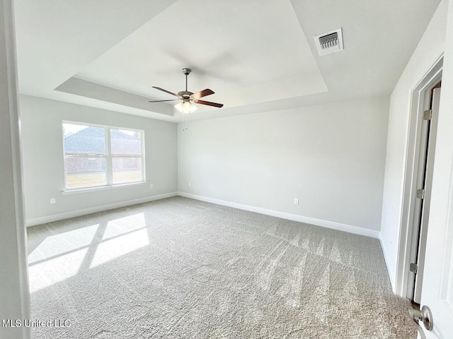 carpeted spare room with visible vents, baseboards, a tray ceiling, and ceiling fan
