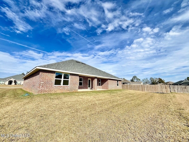 back of house featuring brick siding, fence, a yard, and a shingled roof