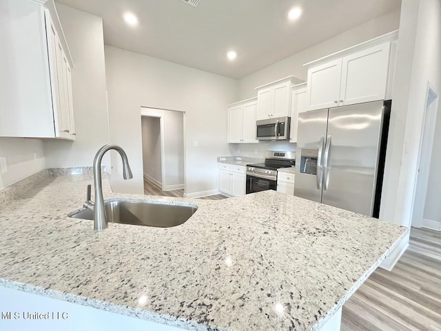 kitchen with white cabinets, appliances with stainless steel finishes, light stone counters, and a sink