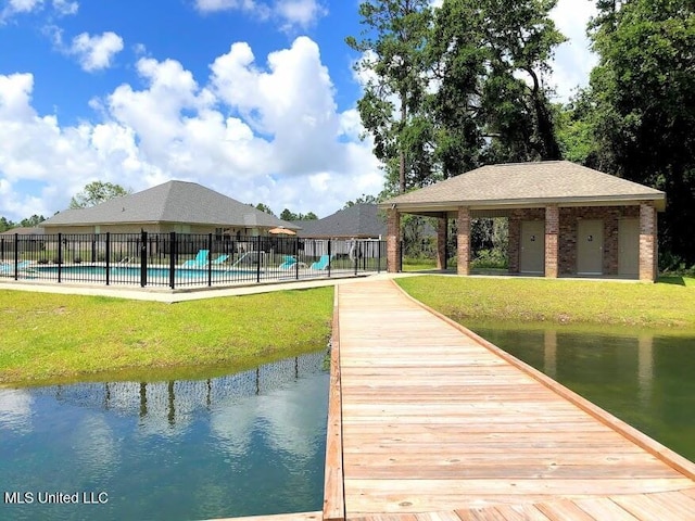 dock area with fence, a water view, and a yard