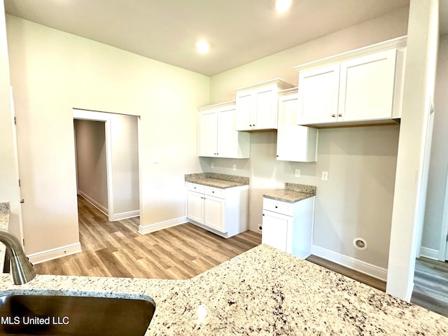 kitchen with light stone counters, light hardwood / wood-style flooring, white cabinetry, and sink