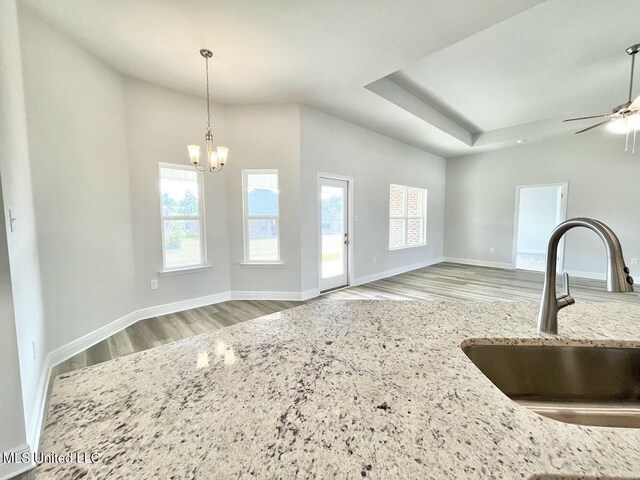 kitchen featuring a sink, baseboards, ceiling fan with notable chandelier, wood finished floors, and light stone countertops