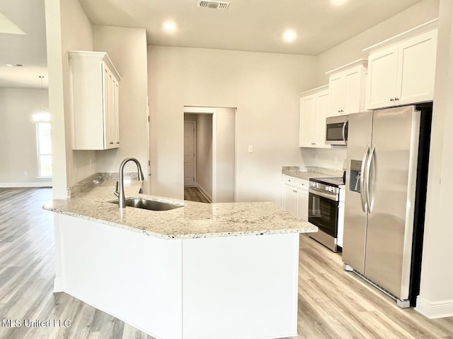 kitchen featuring light wood finished floors, stainless steel appliances, a peninsula, and a sink