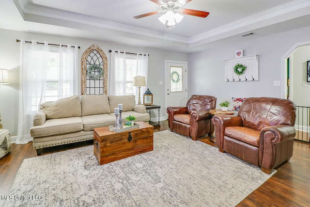 living room featuring ornamental molding, dark wood-type flooring, a raised ceiling, and ceiling fan