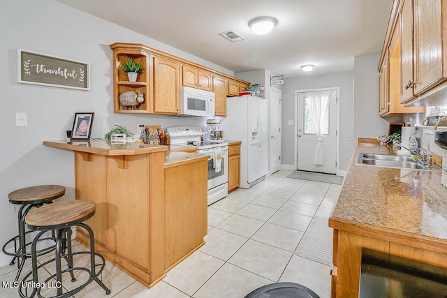 kitchen with kitchen peninsula, light tile patterned floors, a kitchen bar, and white appliances