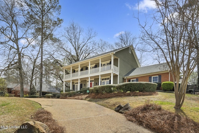 view of front of house with a front yard, a balcony, a porch, and brick siding