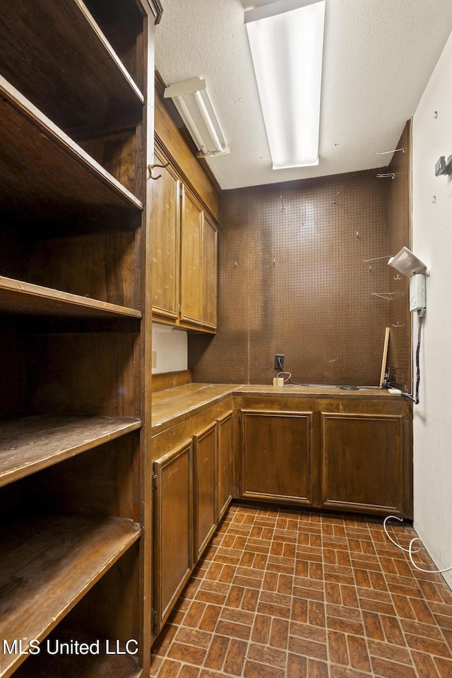 interior space featuring open shelves, brown cabinetry, brick floor, and a textured ceiling