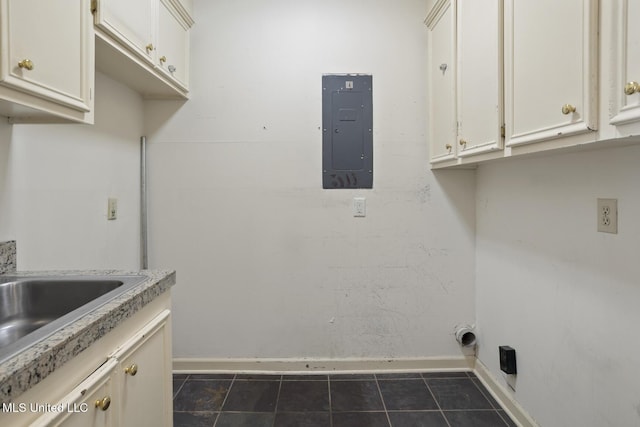 laundry area featuring electric panel, baseboards, dark tile patterned flooring, and a sink