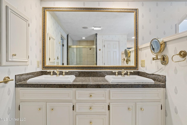 bathroom with wallpapered walls, double vanity, a stall shower, and a sink