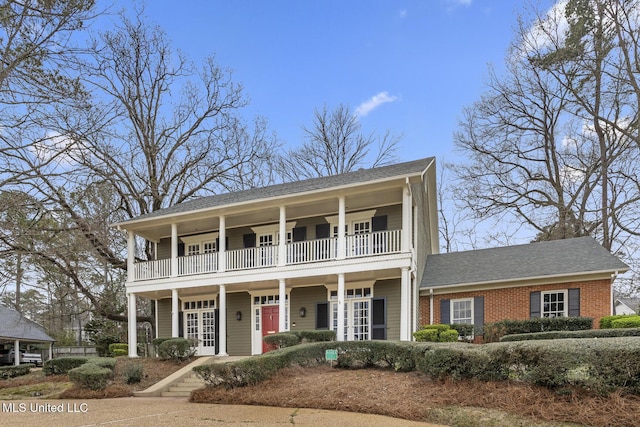 view of front of house featuring a balcony, french doors, brick siding, and roof with shingles