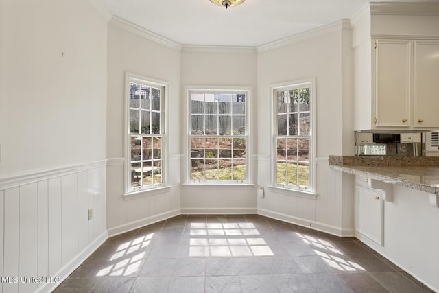 unfurnished dining area with light tile patterned flooring, wainscoting, and crown molding