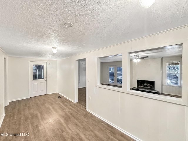 spare room with a fireplace with raised hearth, baseboards, wood finished floors, a textured ceiling, and a ceiling fan