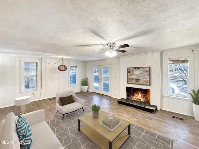 living room with ceiling fan, a lit fireplace, wood finished floors, and a textured ceiling