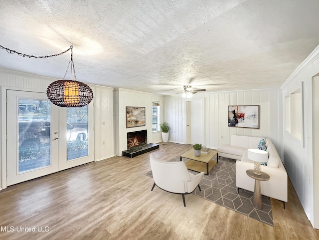 living area featuring wood finished floors, ceiling fan, ornamental molding, a lit fireplace, and a textured ceiling