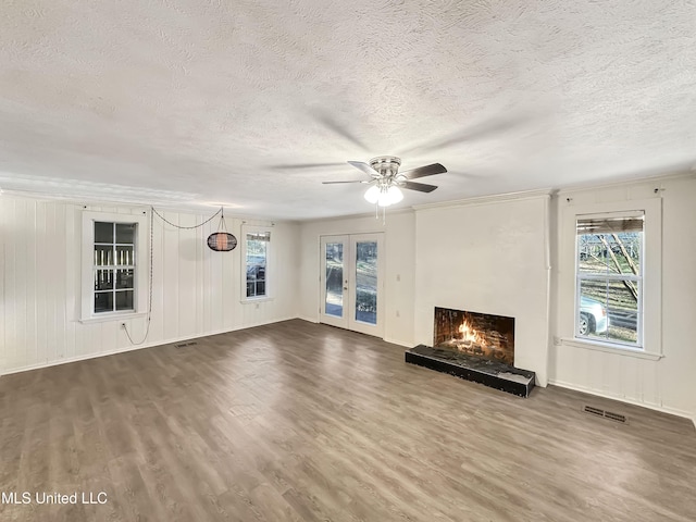 unfurnished living room with ceiling fan, dark wood finished floors, a warm lit fireplace, french doors, and a textured ceiling