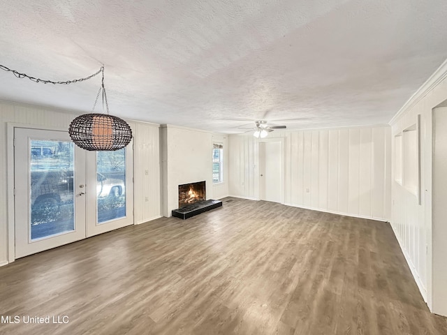 unfurnished living room with a textured ceiling, a lit fireplace, wood finished floors, and a ceiling fan