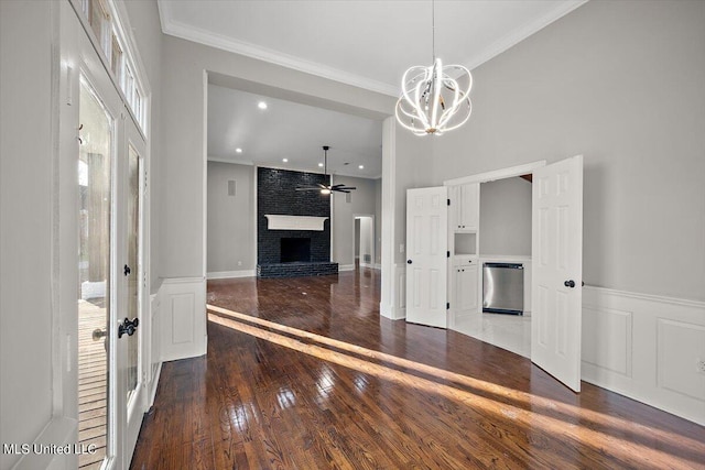 interior space with crown molding, a brick fireplace, hardwood / wood-style flooring, and ceiling fan with notable chandelier