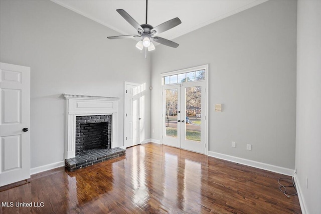 unfurnished living room with a towering ceiling, french doors, a brick fireplace, ceiling fan, and dark wood-type flooring